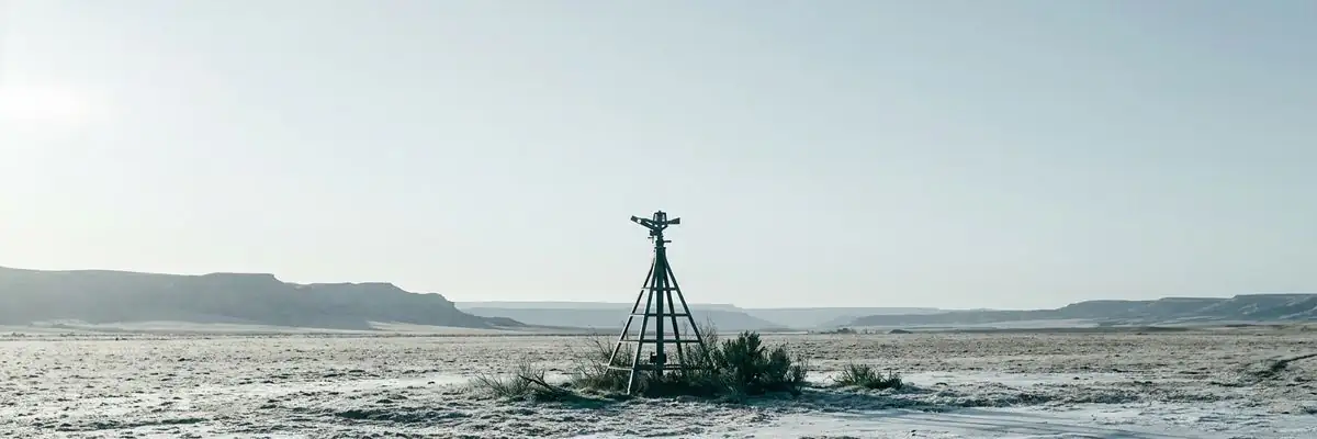 An illustration of a single bare irrigation pipe standing in frozen open ground, frost on the soil crust, in flat low light.